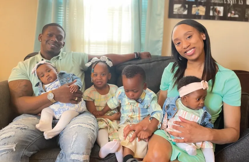 A man and a Woman sitting on a couch with 4 young children.